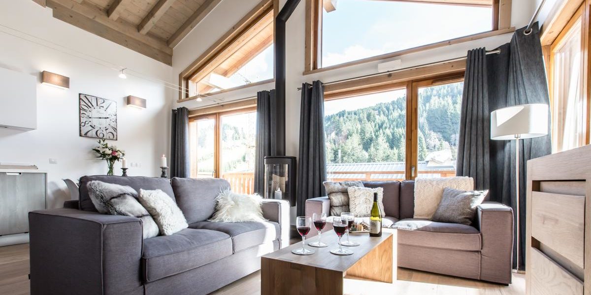 Alpine Residences Les Gets Les Portes du Soleil Frankrijk wintersport skivakantie luxe Kailash living banken kussens wijn wijnglazen klok bloemen houtkachel hoge ramen