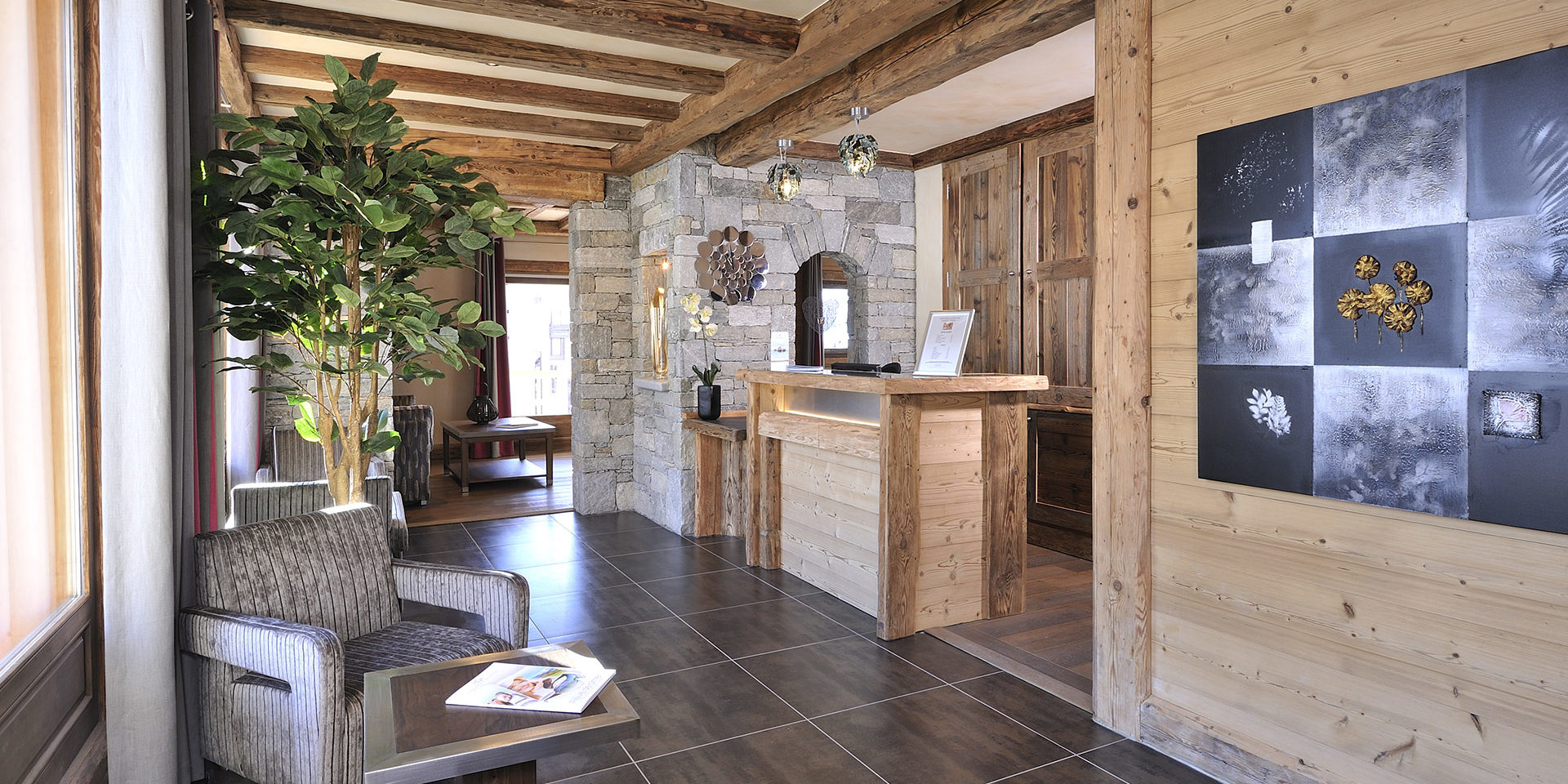 CGH Le Jhana Tignes Tignes-Val d'Isere Frankrijk wintersport skivakantie luxe receptie hout fauteuil boek plant schilderij houten balken