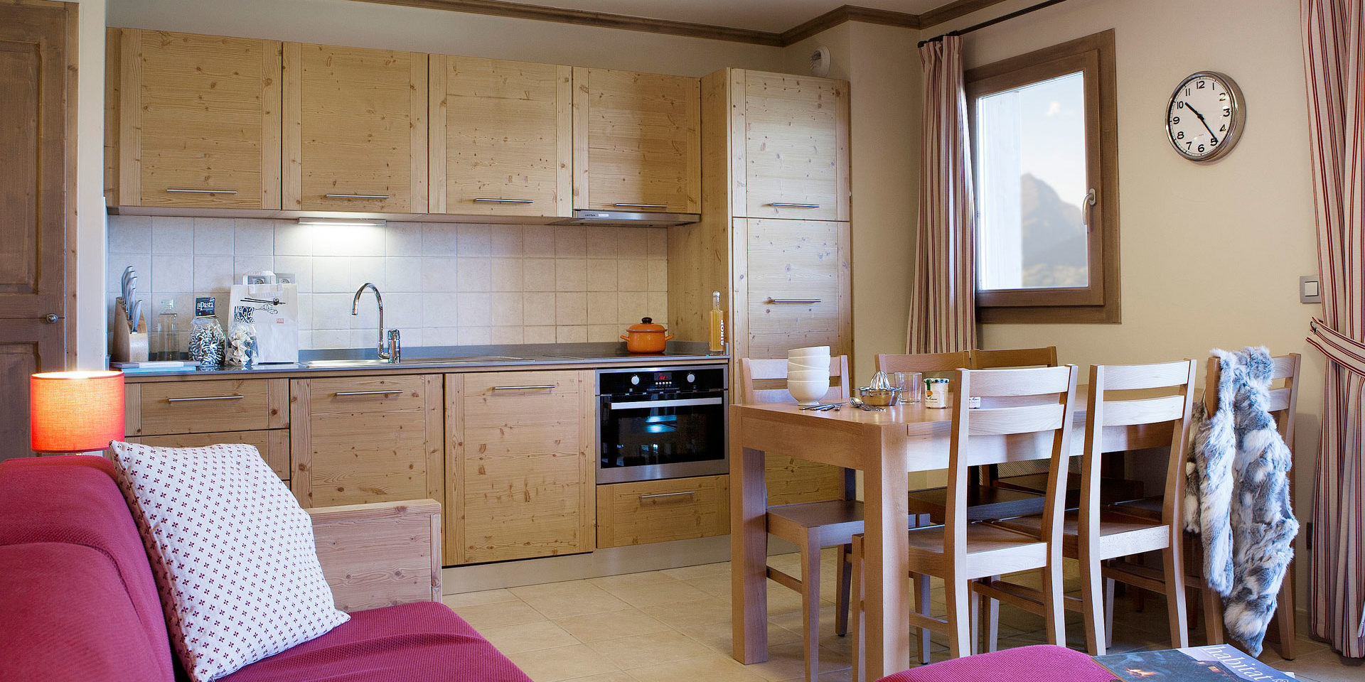 CGH Le Ruitor Sainte Foy Sainte Foy Tarentaise Frankrijk wintersport skivakantie luxe rode bank eettafel stoelen klok houten keuken raam bergen