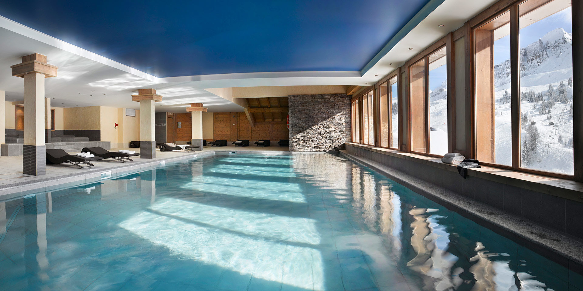 CGH Le Village de Lessy Le Grand Bornand Aravis Frankrijk wintersport skivakantie luxe zwembad ligstoelen handdoeken ramen besneeuwde bergen bomen ontspannen genieten relaxen