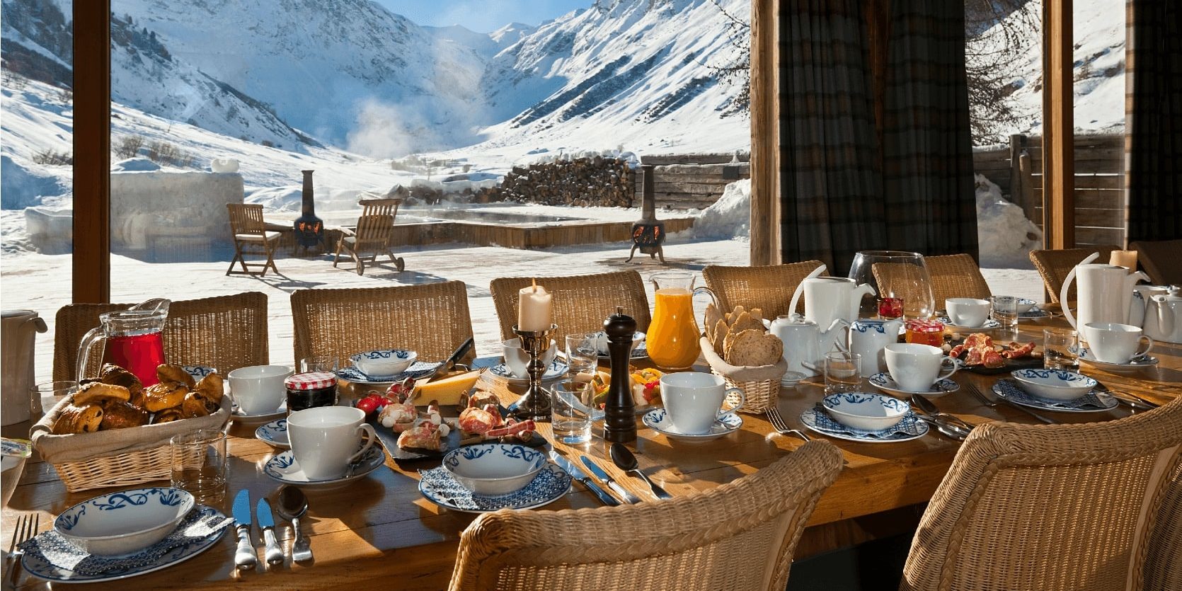Chalet Le Chardon Val d'Isere Tignes-Val d'Isere Frankrijk wintersport skivakantie luxe eetkamer gedekte tafel ontbijt kaarsen raam ligstoelen houtkachel besneeuwde bergen