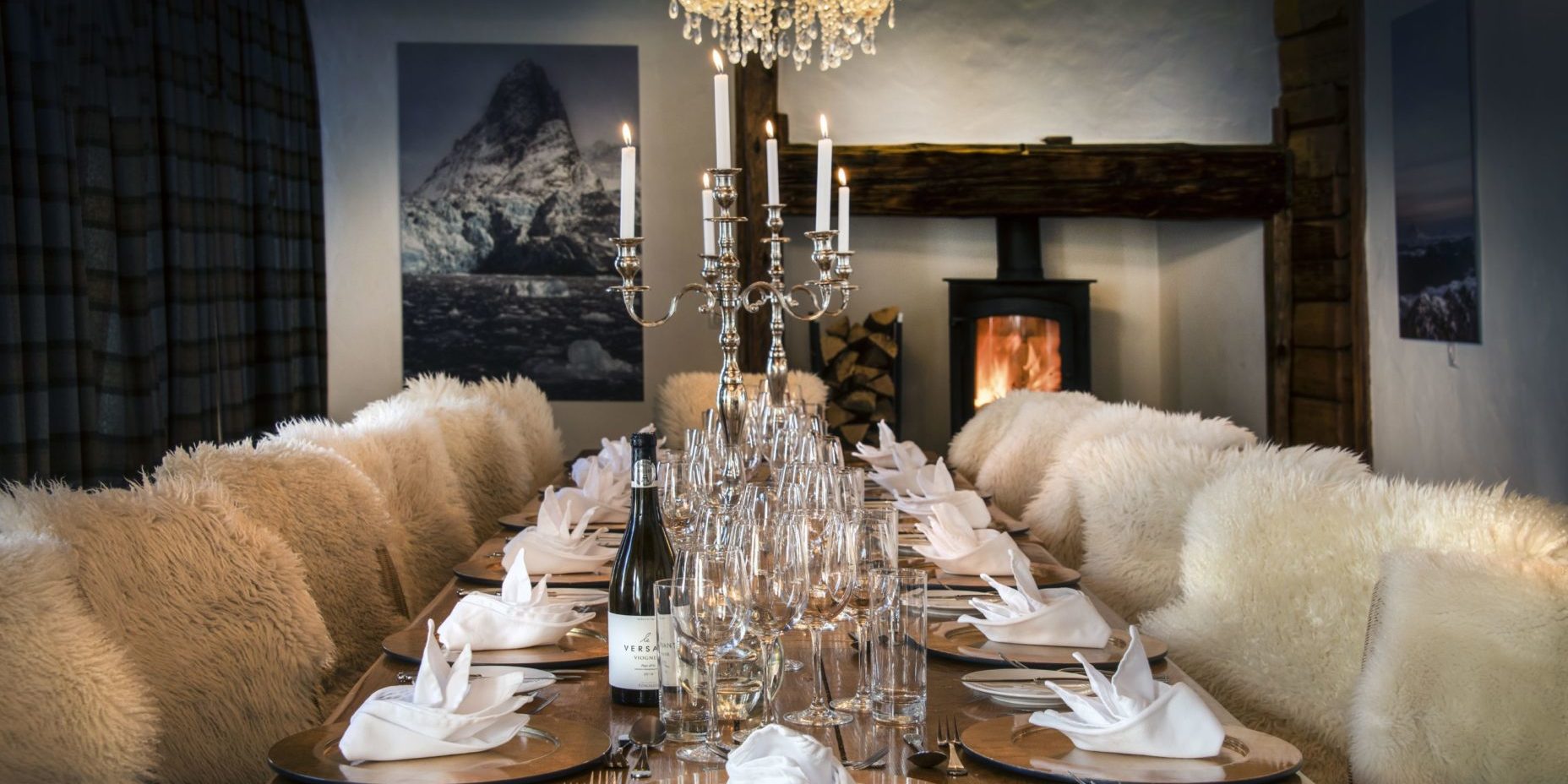 Chalet Le Chardon Val d'Isere Tignes-Val d'Isere Frankrijk wintersport skivakantie luxe eetkamer gedekte tafel wijn wijnglazen kandelaar kaarsen open haard schilderij