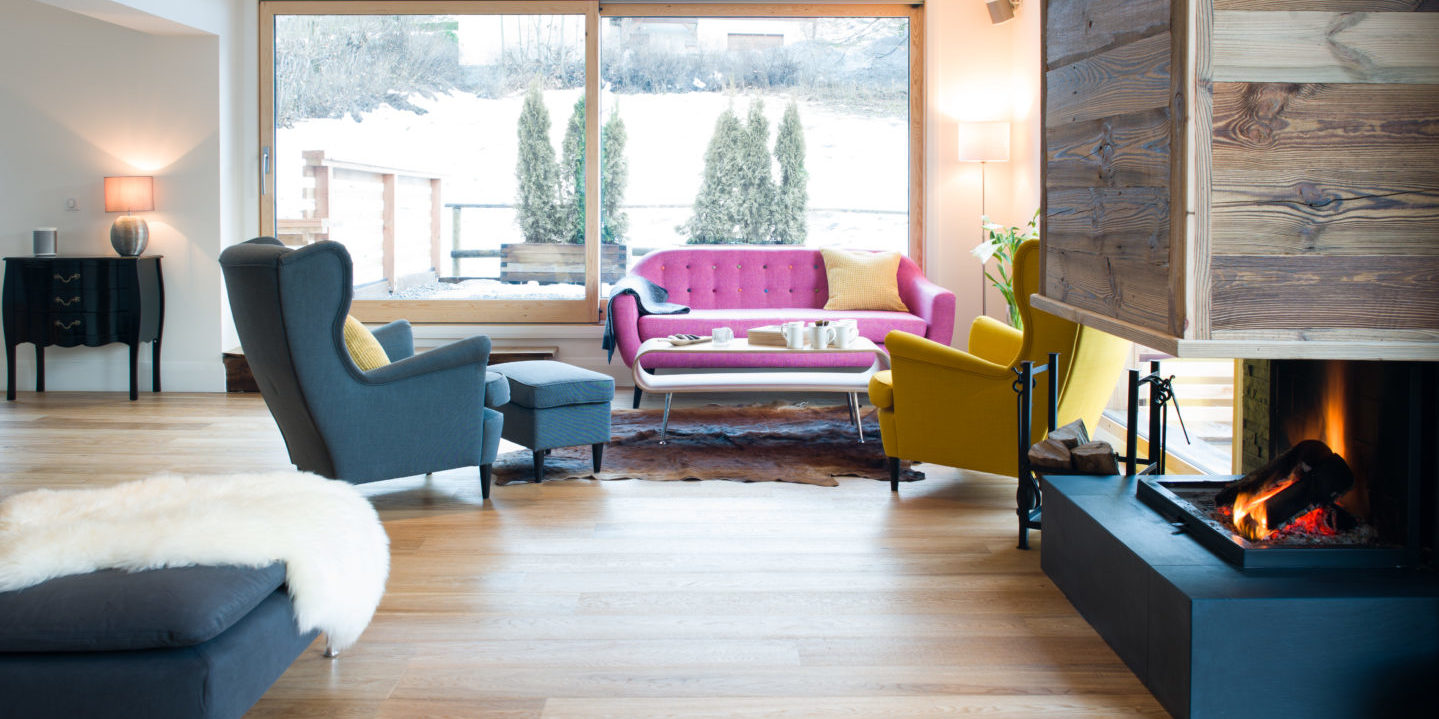 Chalet Rubicon Les Houches Chamonix Mont Blanc Frankrijk wintersport skivakantie luxe living zithoek open haard roze bank gele fauteuil blauwe fauteuil hocker vloerkleed ramen