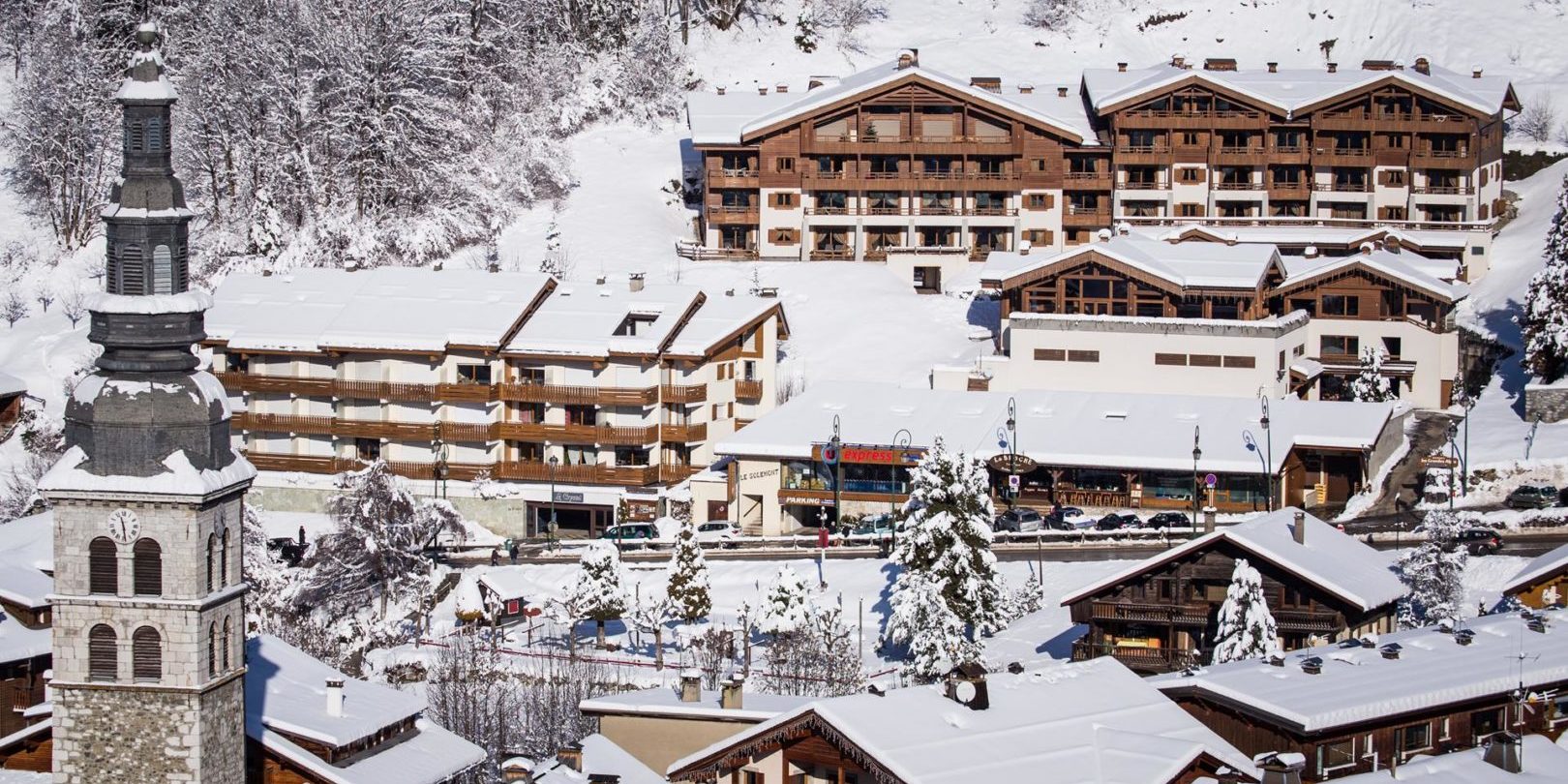Residence Les Grandes Alpes La Clusaz Aravis Frankrijk wintersport skivakantie luxe ligging residence besneeuwde bomen kerk bergen